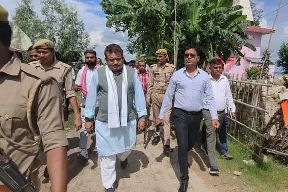 Walking along a village lane with officials and police personnel during the visit